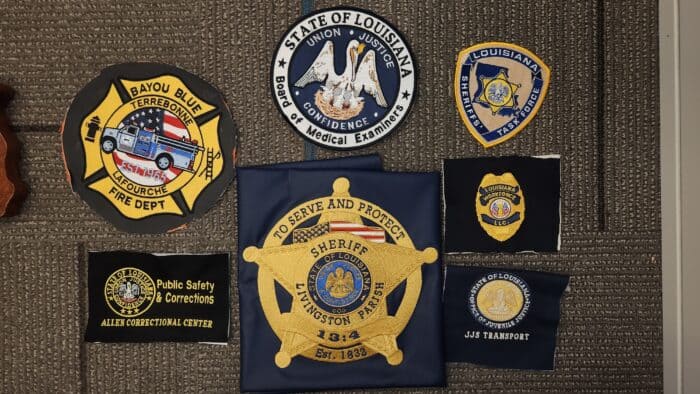 A collection of eight various law enforcement and public safety patches from Louisiana displayed on a gray surface.