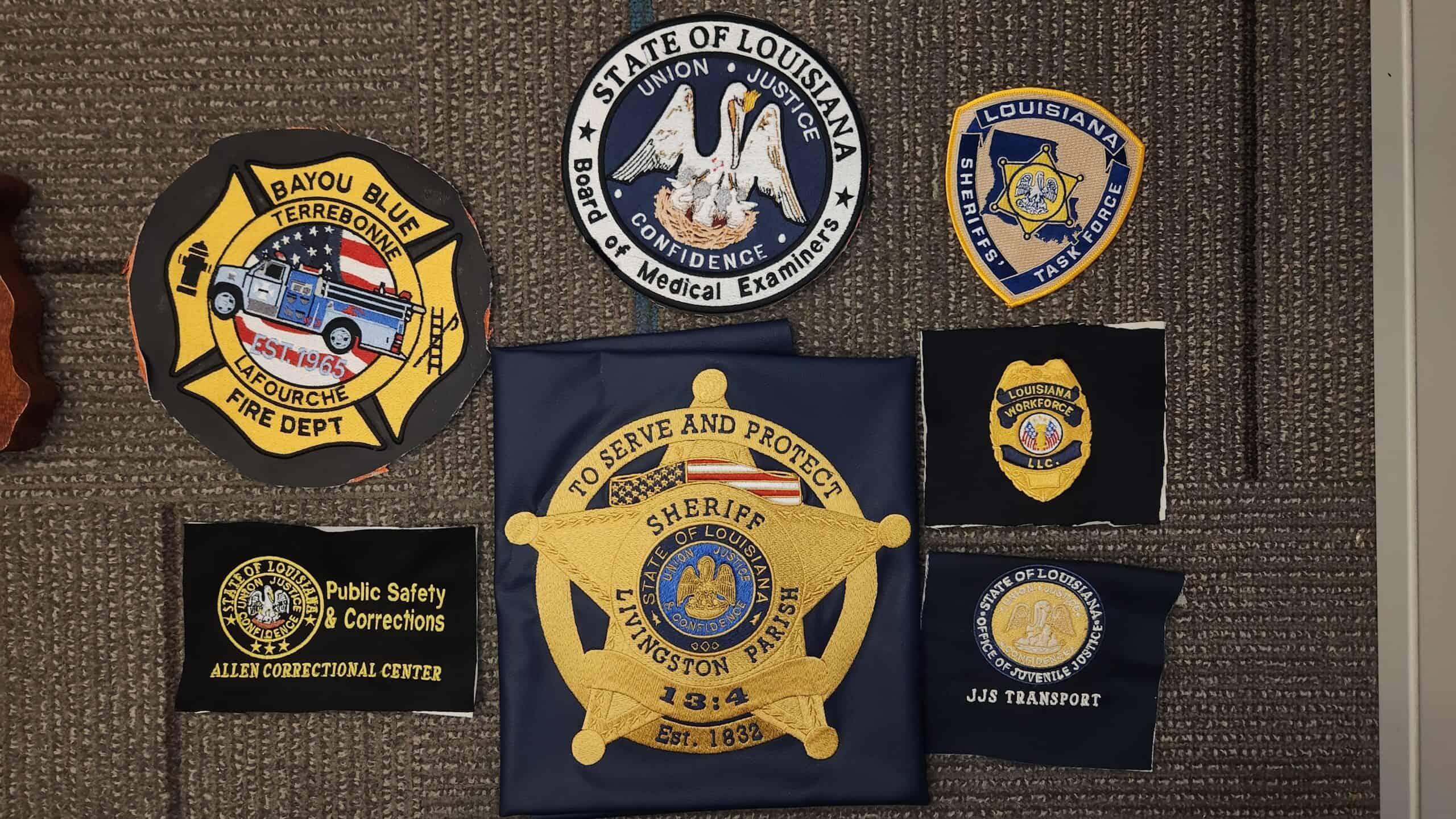 A collection of eight various law enforcement and public safety patches from Louisiana displayed on a gray surface.