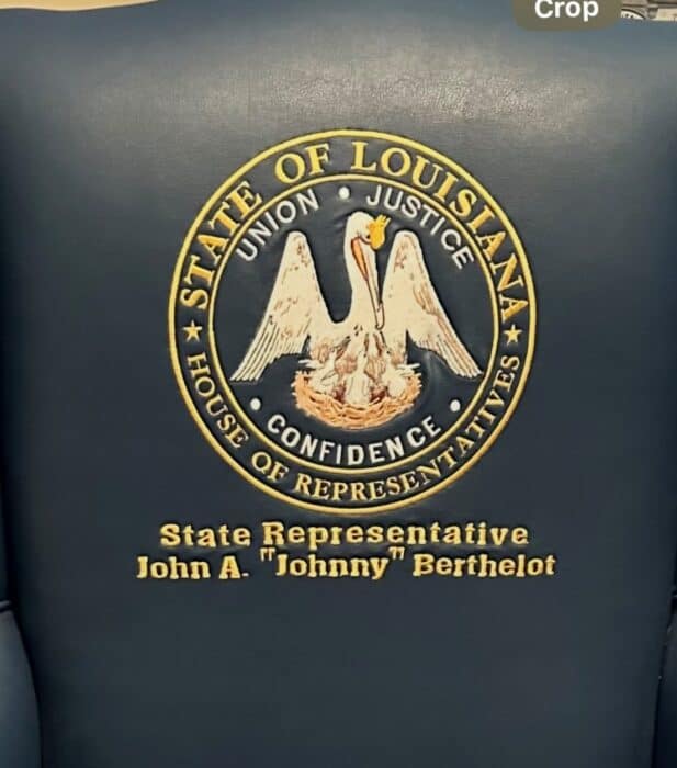 Close-up of a blue leather chair with the Louisiana House of Representatives seal and the name John A. "Johnny" Berthelot embroidered in gold.