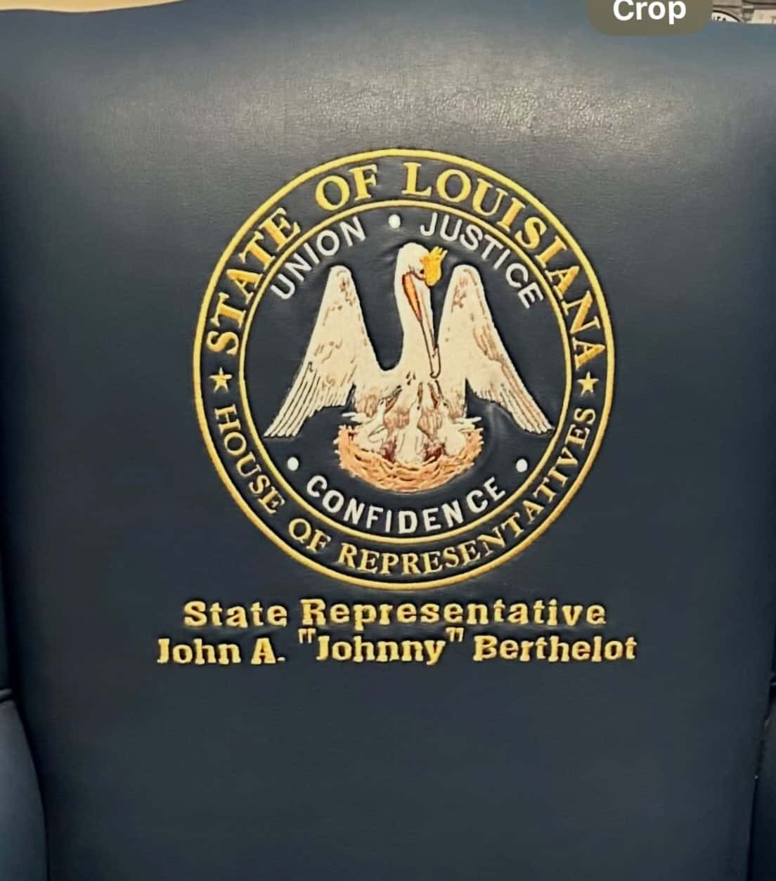 Close-up of a blue leather chair with the Louisiana House of Representatives seal and the name John A. "Johnny" Berthelot embroidered in gold.