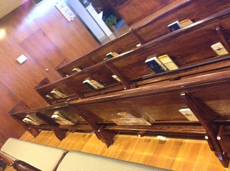 Wooden church pews with hymnals and Bibles in racks, viewed at an angle, on a polished wood floor.