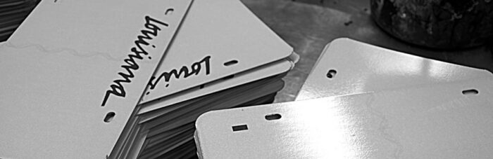 Stacks of blank license plates, some with "Louisiana" written on them, are arranged on a flat surface in black and white.