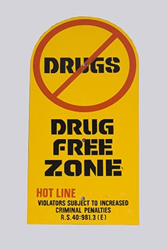 A Metal Sign: yellow, red crossed-out circle over "DRUGS," says "DRUG FREE ZONE" with legal warning in black and red.
