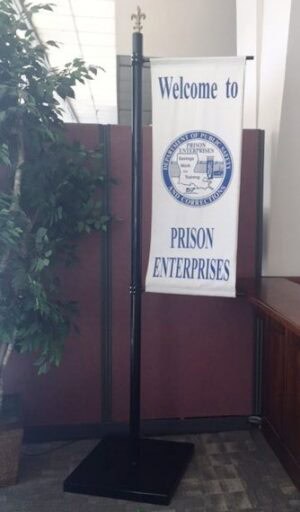 A Vertical Banner Pole (8') holds a "Welcome to PRISON ENTERPRISES" banner by a potted plant and maroon partition wall.