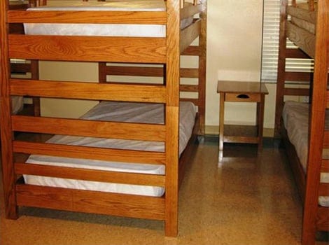 Two wooden bunk beds with white mattresses are placed parallel to each other, with a small wooden nightstand in between.