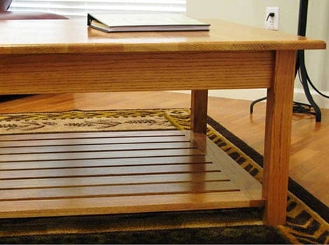 A wooden coffee table with a slatted lower shelf, a book on top, and a rug underneath.