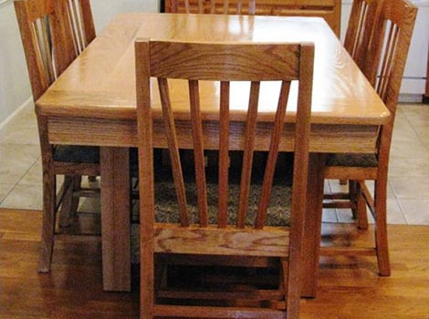 A wooden dining table with six matching wooden chairs arranged around it on a hardwood floor.