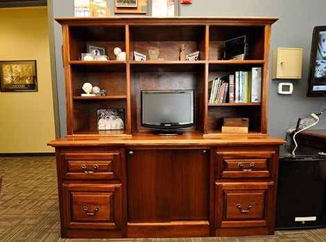 A wooden entertainment center with shelves, books, decor items, and a small flat-screen TV in the center.