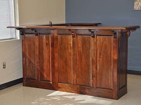 A wooden counter with a polished finish stands against a blue and beige wall near a window with sunlight casting shadows.