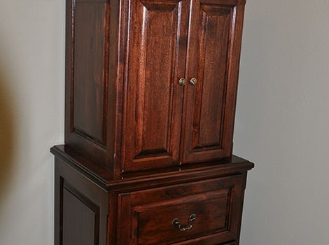 A dark wooden cabinet with two paneled doors on top and a single drawer with metal handles below, set against a plain light-colored wall.
