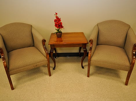 Two upholstered armchairs sit on either side of a wooden side table with a small red flower arrangement on top.