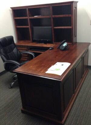 A 6' Desk with return 72x30x30 holds a book, phone, monitor, and black office chair in a compact office space.
