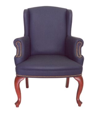 The PE Wingback Guest Chair features navy blue fabric, wooden legs, and brass nailhead trim on the arms and seat.