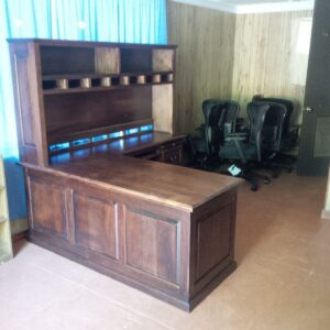 A Hutch, Return 78x13x40 L-shaped desk sits in a wood-paneled room with three black office chairs in the corner.