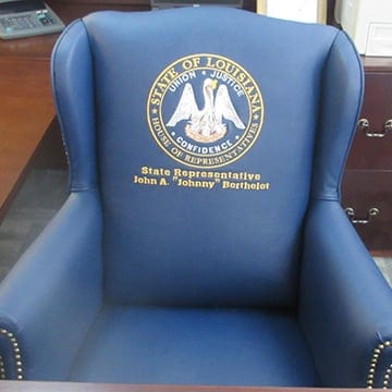 Blue upholstered chair with the Louisiana state seal and text for State Representative John A. "Johnny" Berthelot on the backrest.