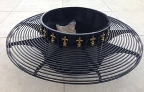 A round black metal tree guard with gold fleur-de-lis designs sits on a tiled surface.